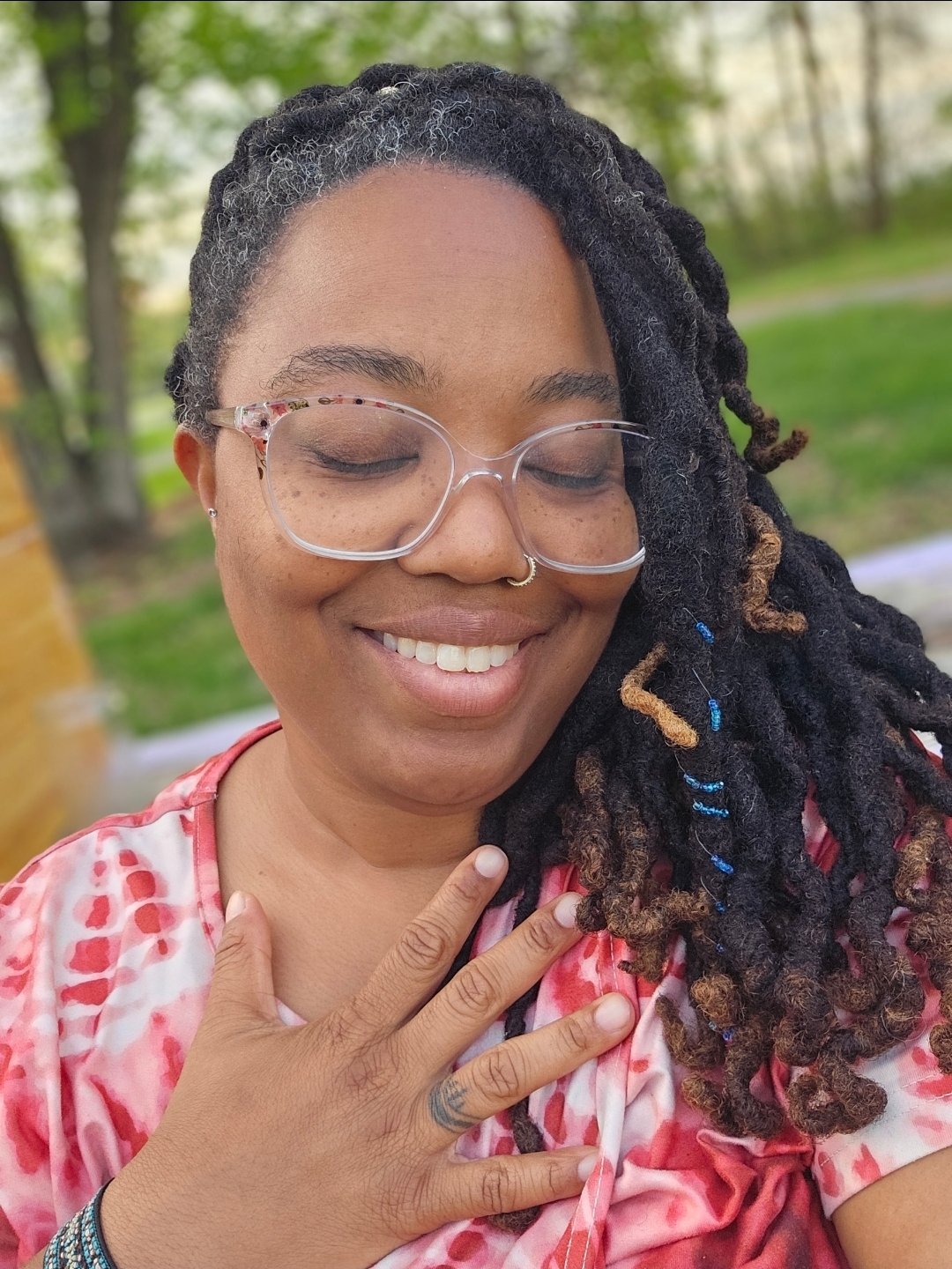 Rashida McCoy outdoors, smiling with her hand over her heart, wearing a pink and red patterned top